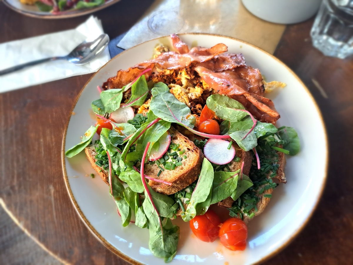 Brunchteller mit Speck, Eierspeis, Blattsalat, Radieschen und Paradeisern auf geröstetem Brot