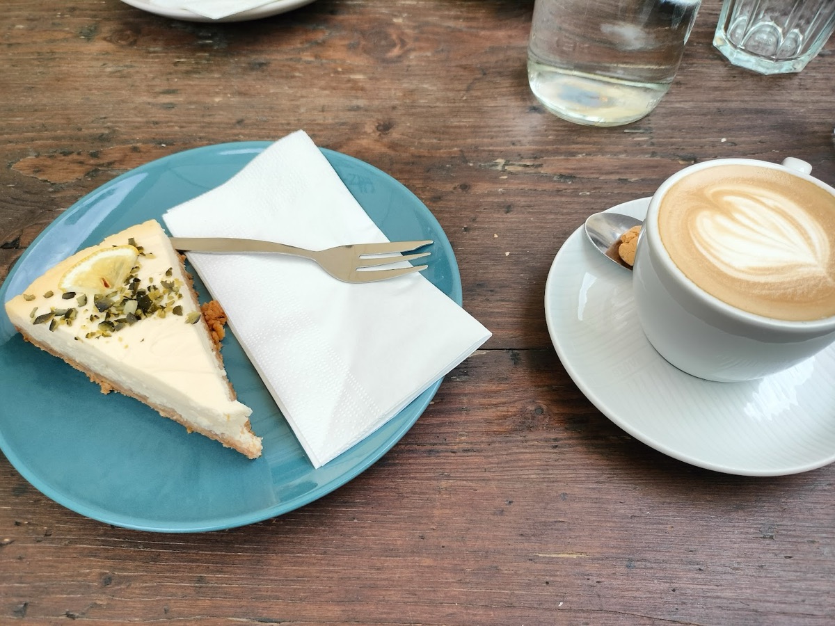 Cheesecake mit Zitrone und Kürbiskernen neben einem Cappuccino auf einem Holztisch