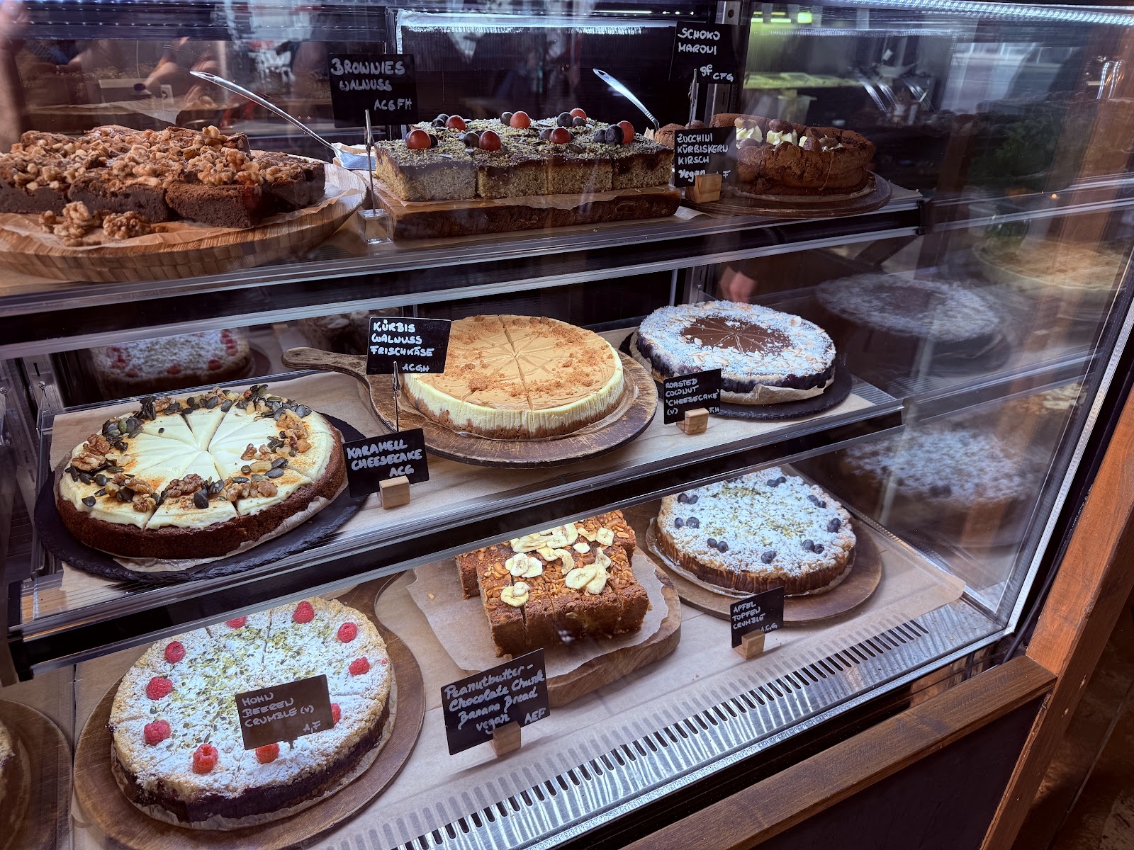 Kuchenvitrine im Cafe 7Stern mit beschrifteten Kreidetafeln: Brownies, Karamell-Cheesecake, Mohn-Beeren-Crumble und vegane Kuchen