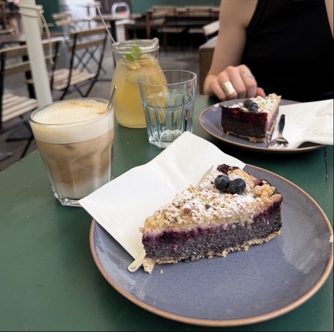 Stück Mohn-Beeren-Kuchen mit Streuseln neben einem Latte auf einem grünen Tisch